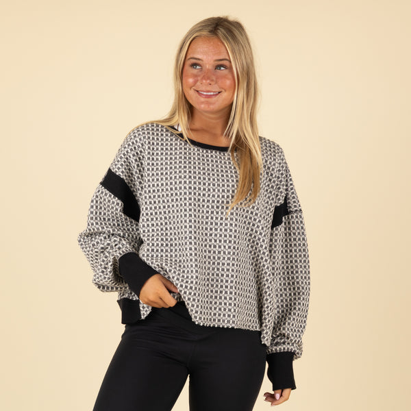Woman wearing a patterned sweater with black sleeves against a beige background
