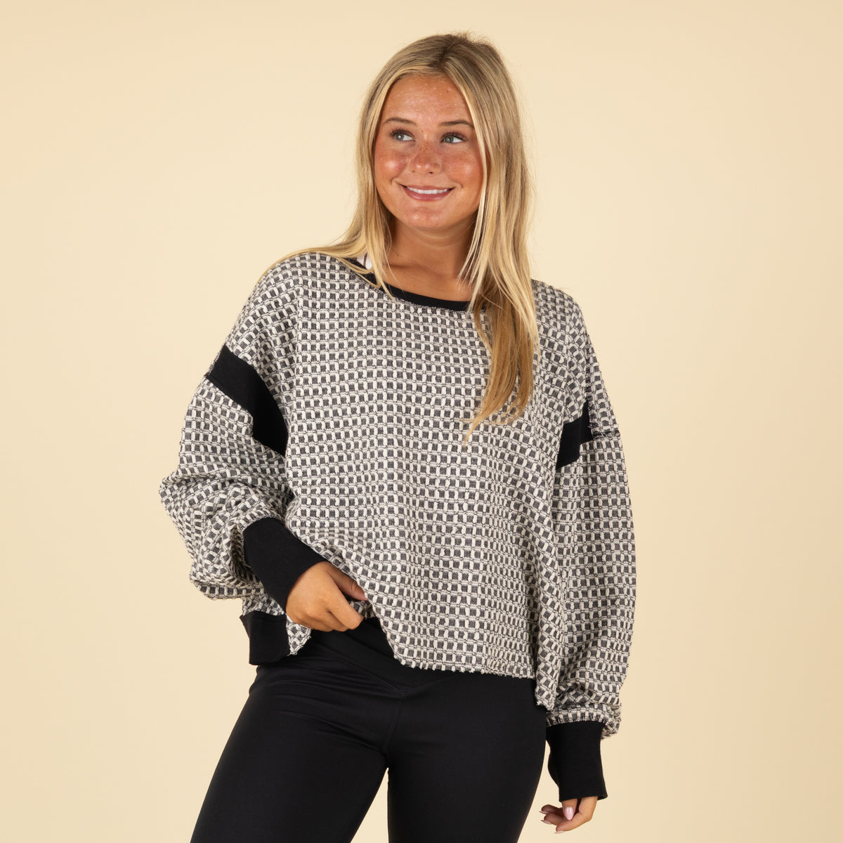 Woman wearing a patterned sweater with black sleeves against a beige background