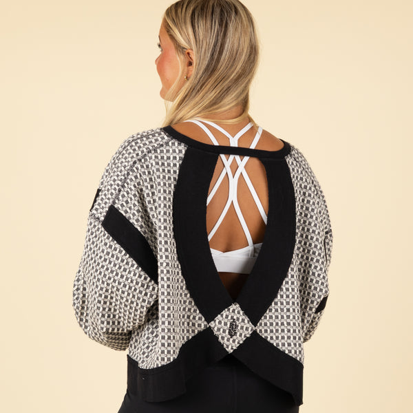 Black and white geometric patterned long-sleeve top with black cuffs and neckline, shown from an angled front view with relaxed sleeves.