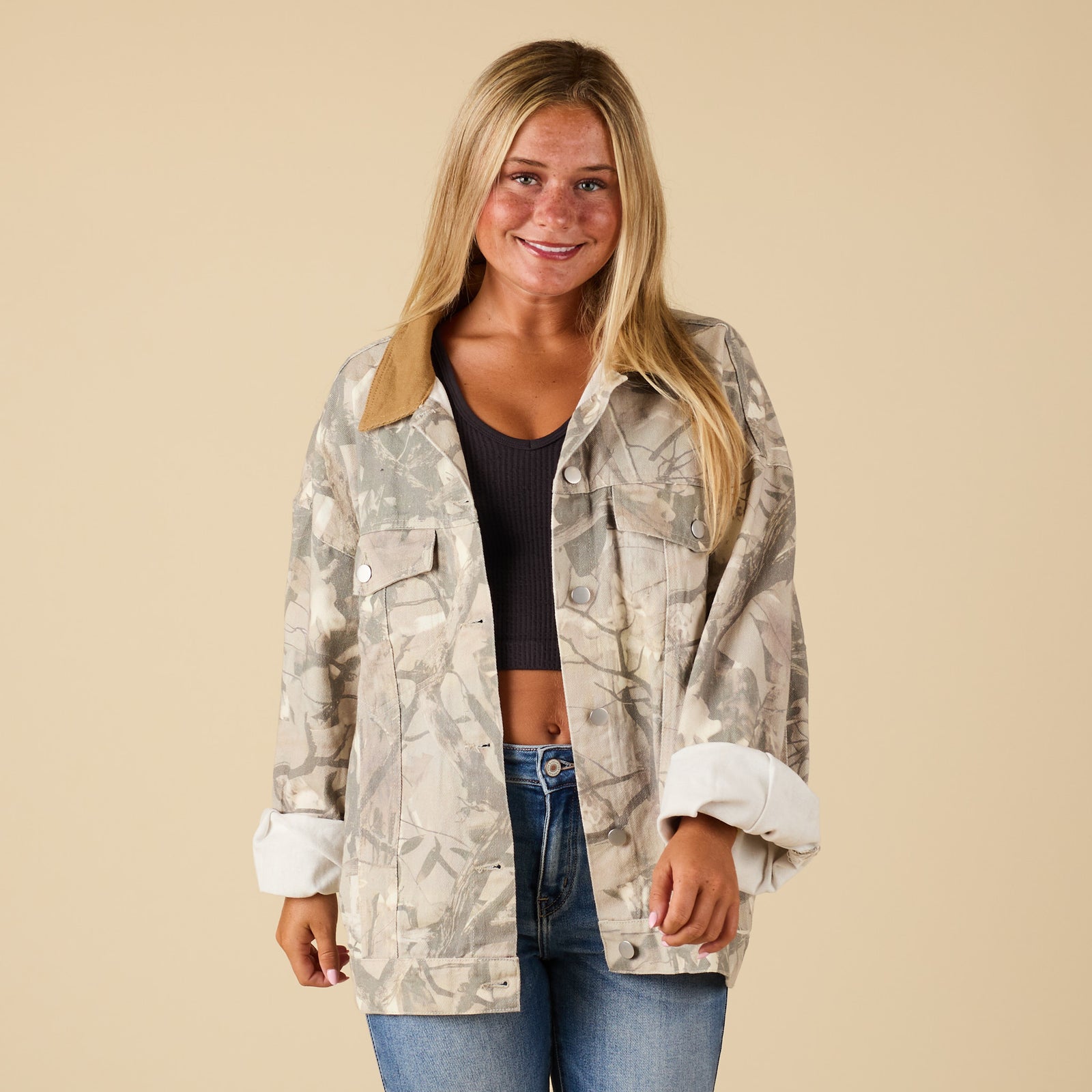 Front view of women’s oversized camo print jacket with button-front and corduroy collar, worn over a black crop top and jeans.