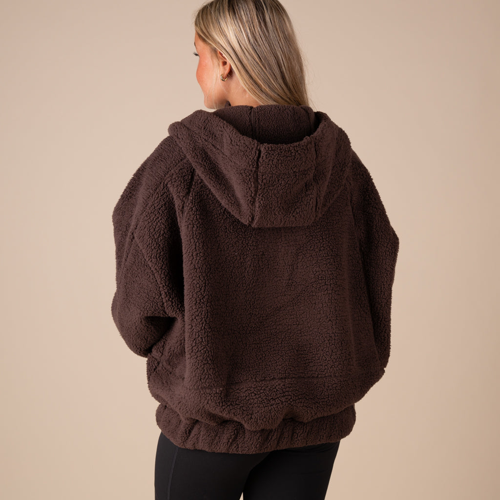 Person wearing a brown fleece hoodie on a beige background