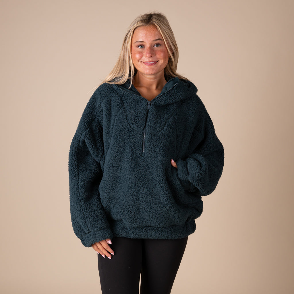 Woman wearing a dark green fleece pullover against a beige background