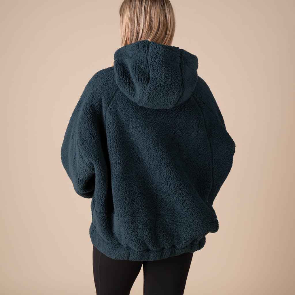 Person wearing a dark green fleece hoodie on a beige background