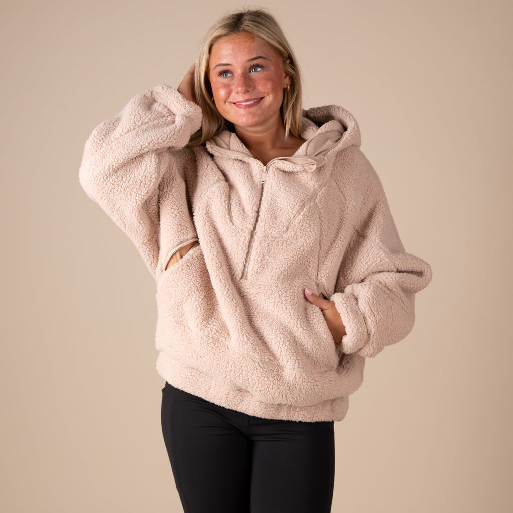 Woman wearing a beige fleece hoodie against a plain background