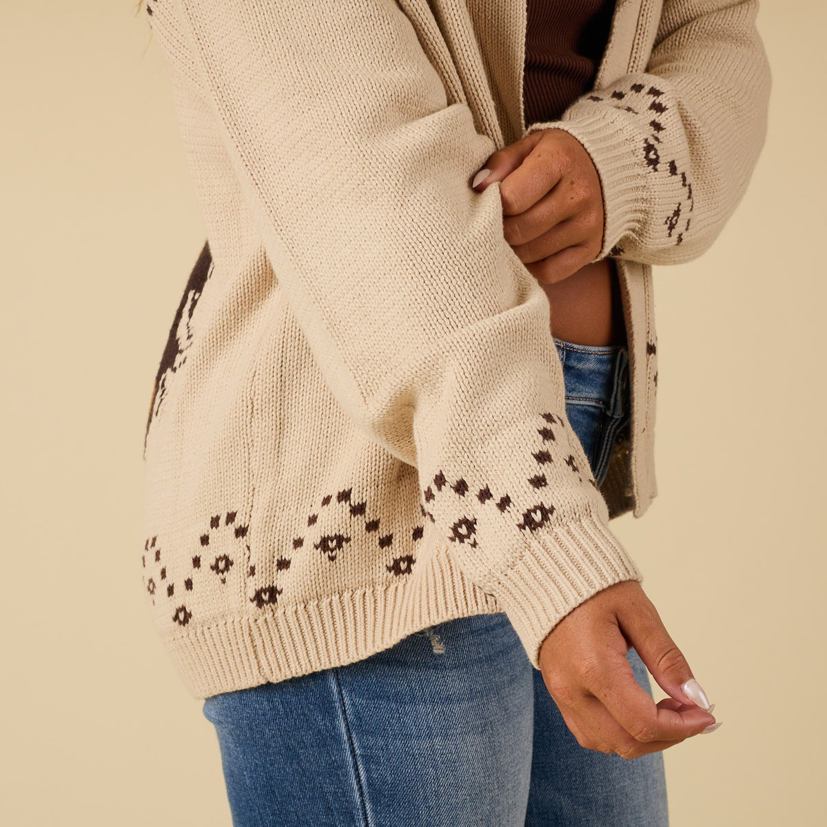 Close-up of cardigan sleeve with brown stitched pattern along cuff and hem.
