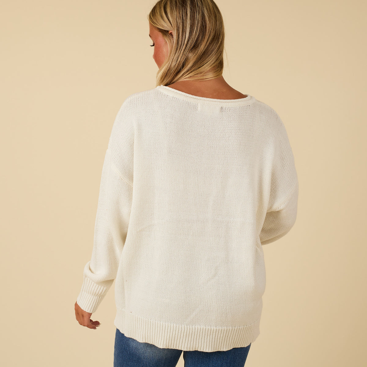Back view of ivory knit sweater with relaxed fit, ribbed hem, and drop shoulders.