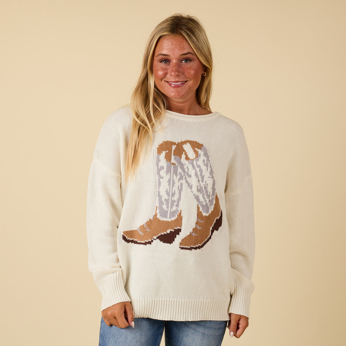 Ivory knit sweater with cowboy boot graphic in tan, gray, and brown, relaxed fit.