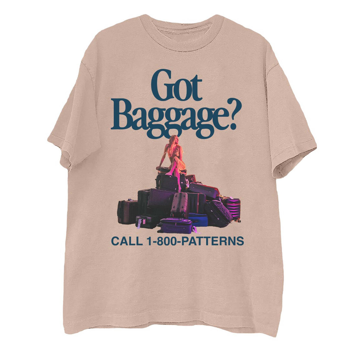 Front view of light pink short sleeve t-shirt with “Got Baggage?” text, woman sitting on stacked luggage, and “Call 1-800-PATTERNS” slogan.