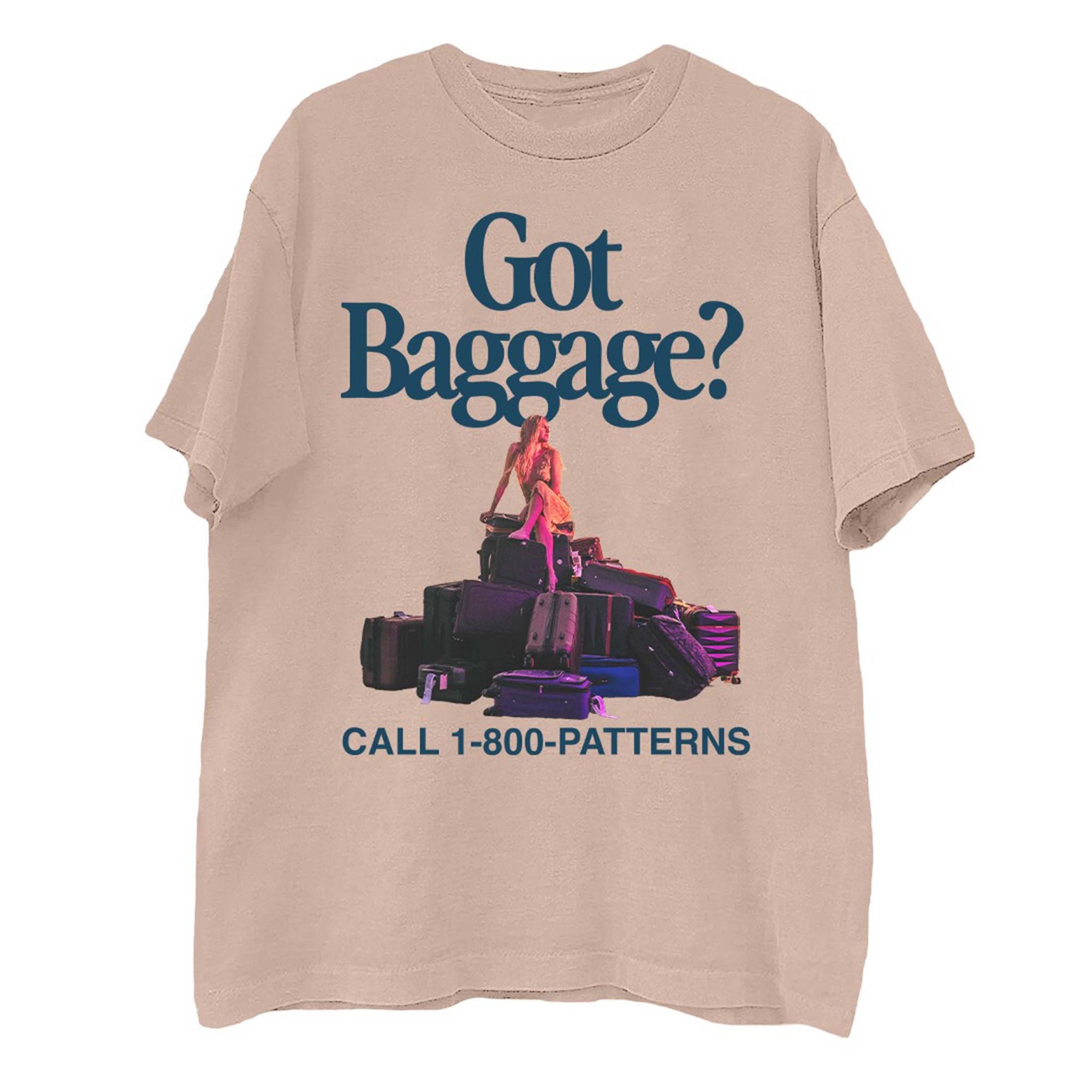 Front view of light pink short sleeve t-shirt with “Got Baggage?” text, woman sitting on stacked luggage, and “Call 1-800-PATTERNS” slogan.