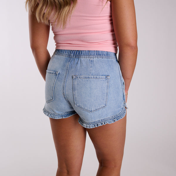 Light wash high-rise denim shorts with ruffle hem detail shown from back view.