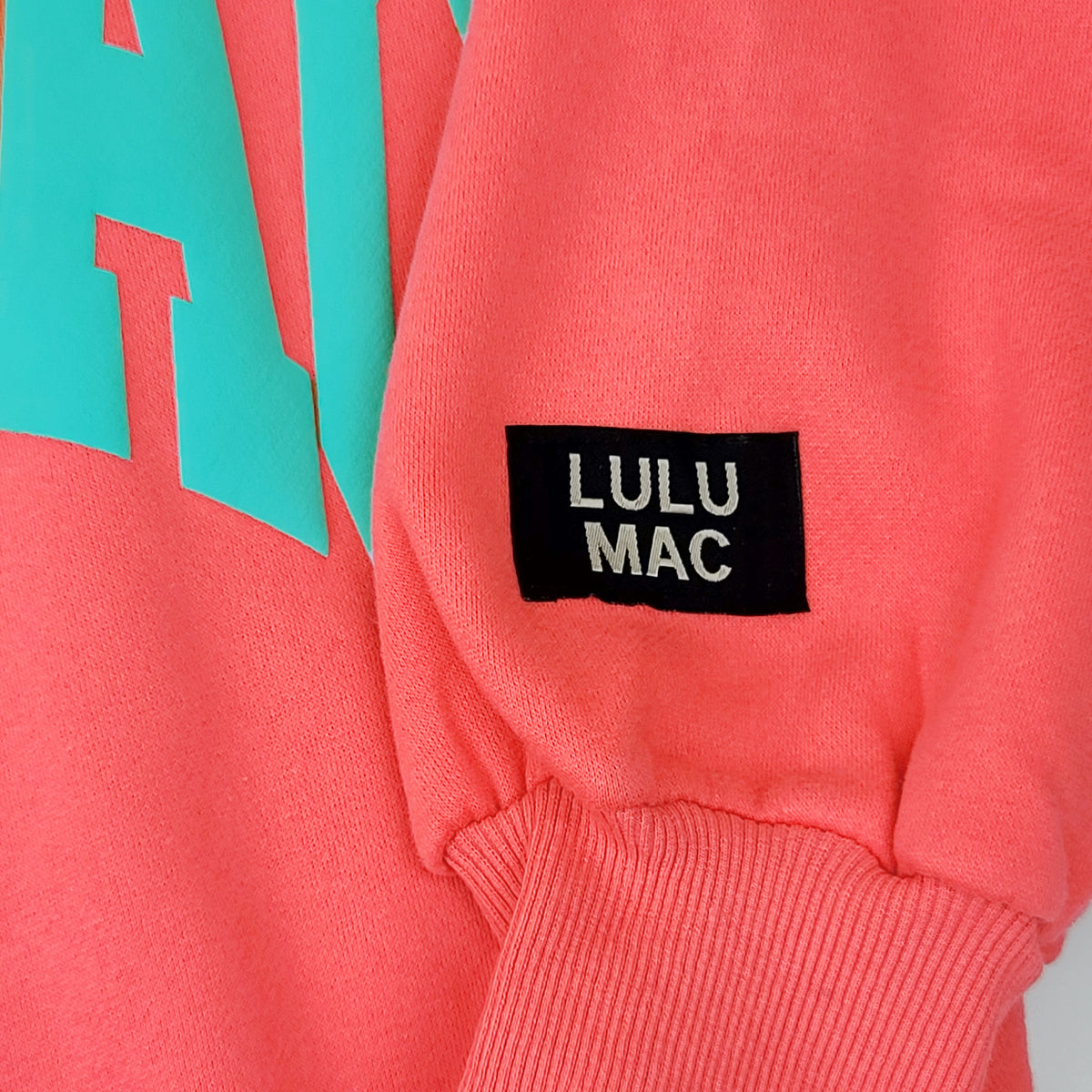 Close-up of a pink sweatshirt with 'LULU MAC' label