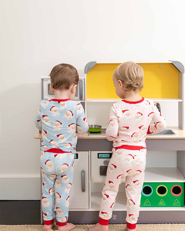 two kids playing with a fake kitchen wearing christmas pajamas