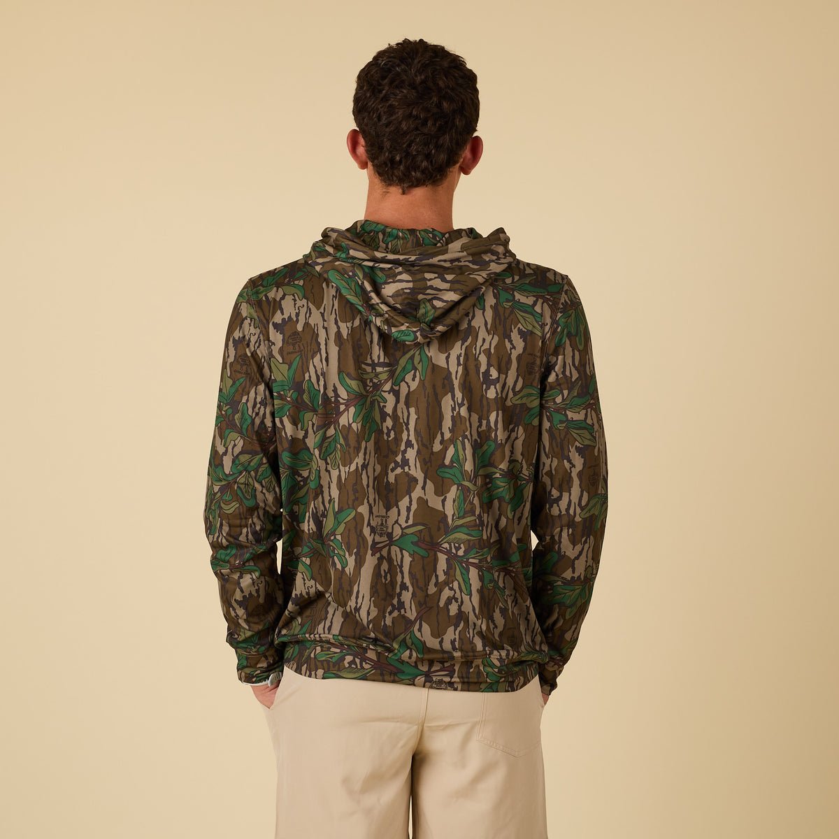 Person wearing a camouflage hoodie on a beige background