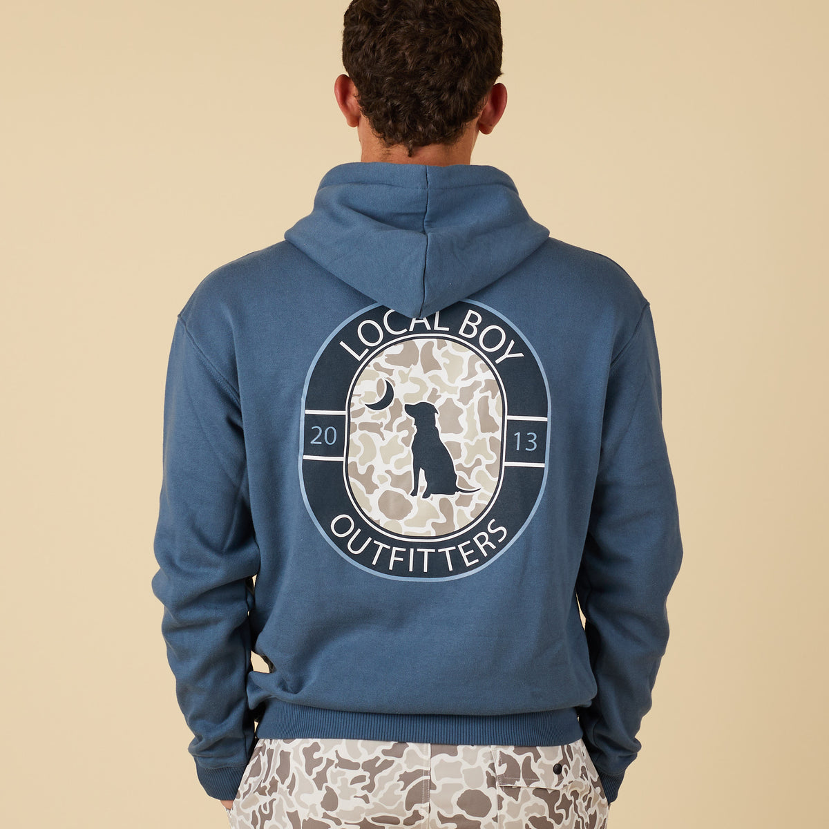Man wearing a blue hoodie with a camo badge graphic on the back.
