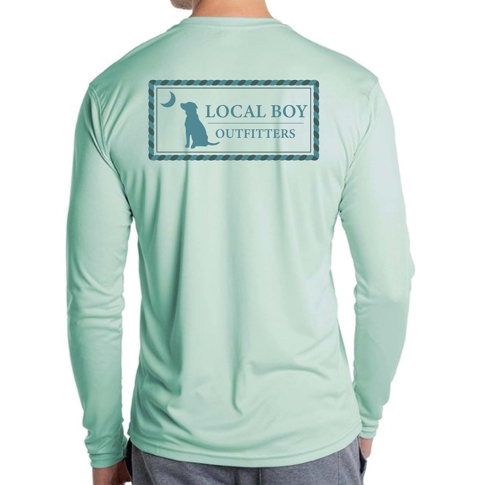Local Boy Outfitters long sleeve performance shirt in seagrass. Back features a rectangular rope-bordered logo with a lab silhouette, crescent moon, and brand name in blue.