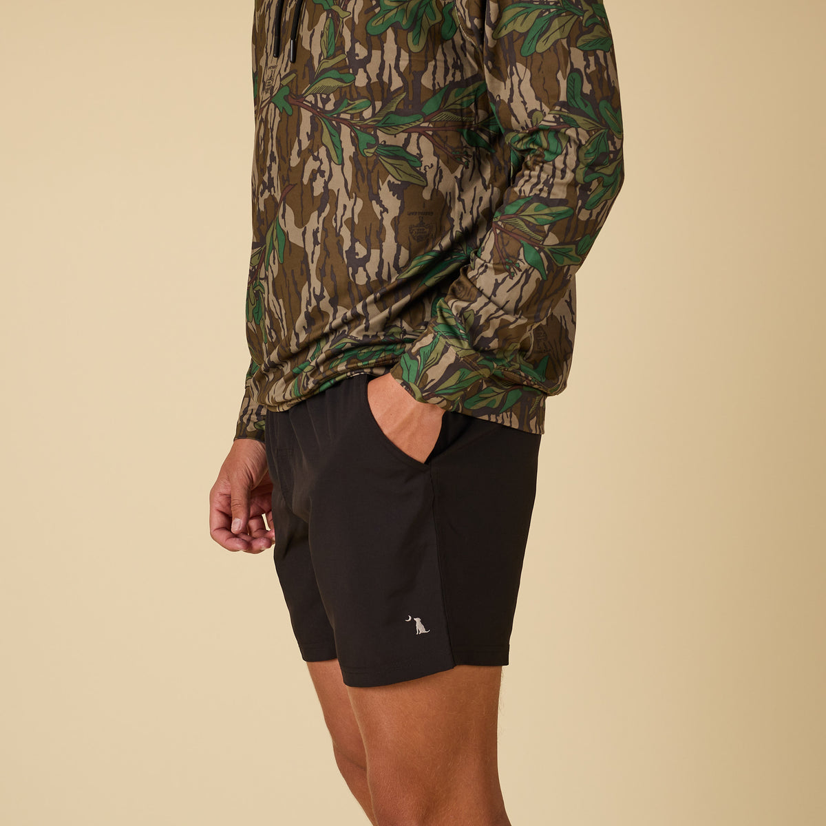 Side view of man wearing a camo performance hoodie with black athletic shorts.