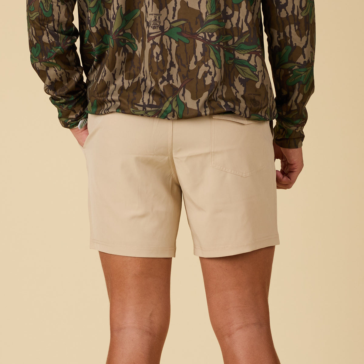 Person wearing beige shorts and a camouflage jacket on a beige background