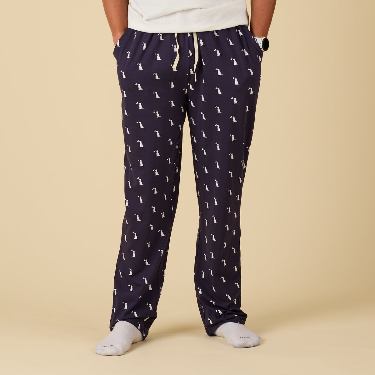Navy blue pajama pants with white dog pattern worn by a person on a beige background