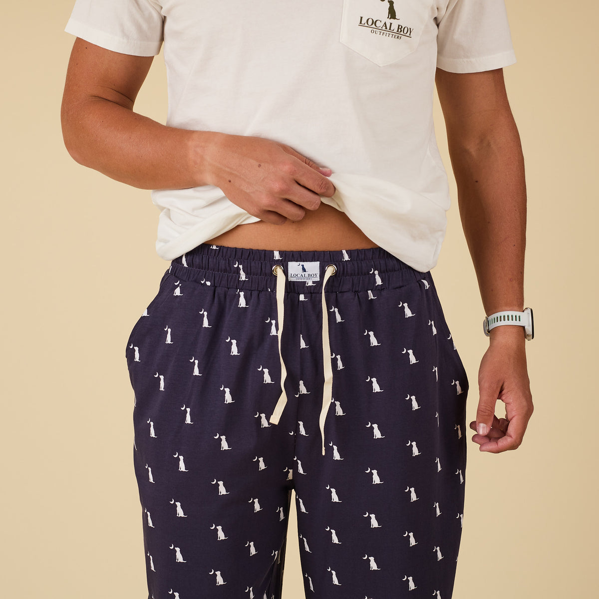 Person wearing navy blue pajama pants with white patterns and a white t-shirt on a beige background