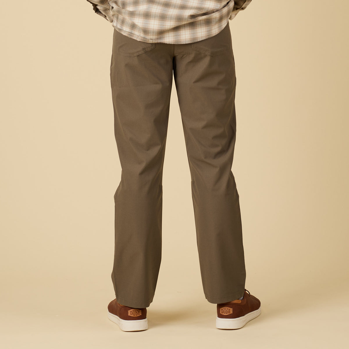 Person wearing olive pants and plaid shirt on a beige background