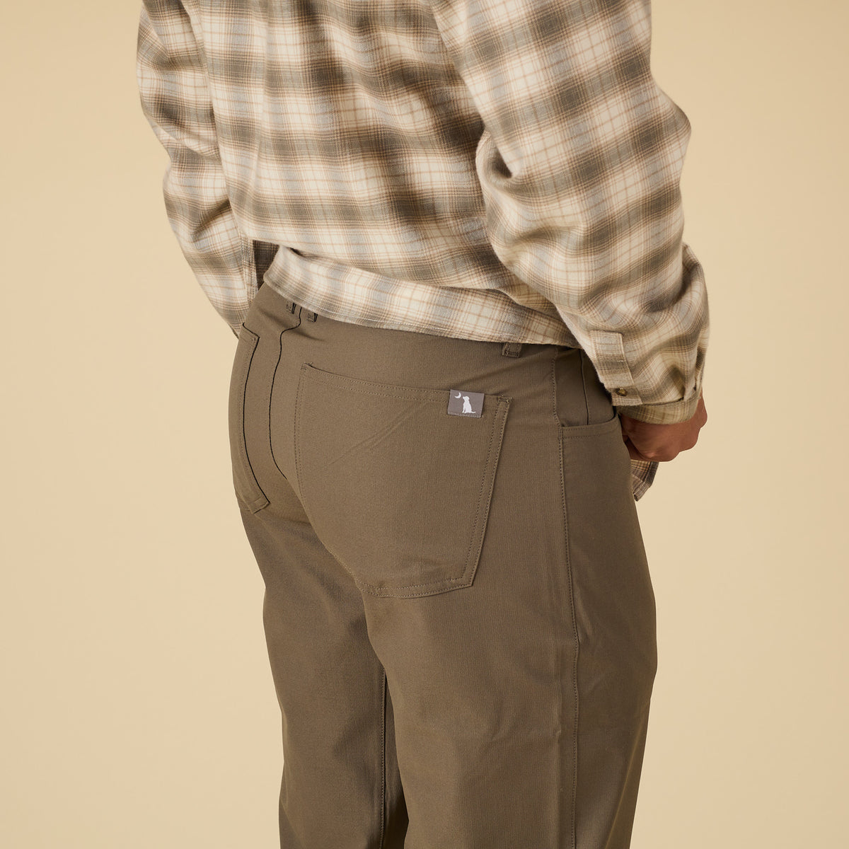 Person wearing a plaid shirt and brown pants on a beige background
