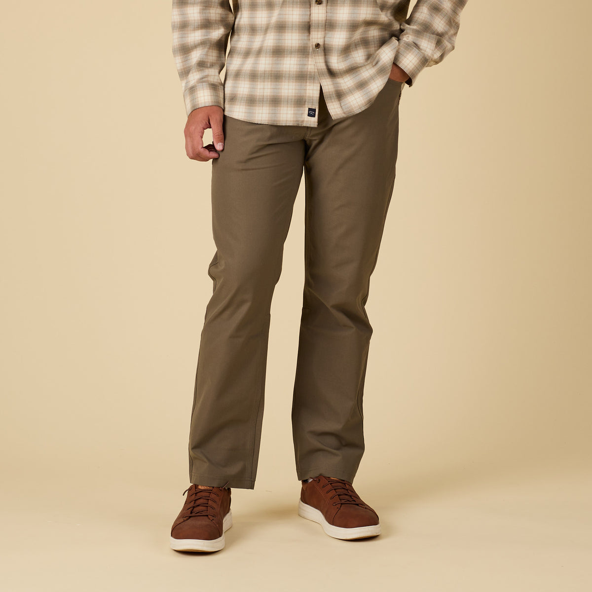 Person wearing a plaid shirt, olive pants, and brown shoes on a beige background