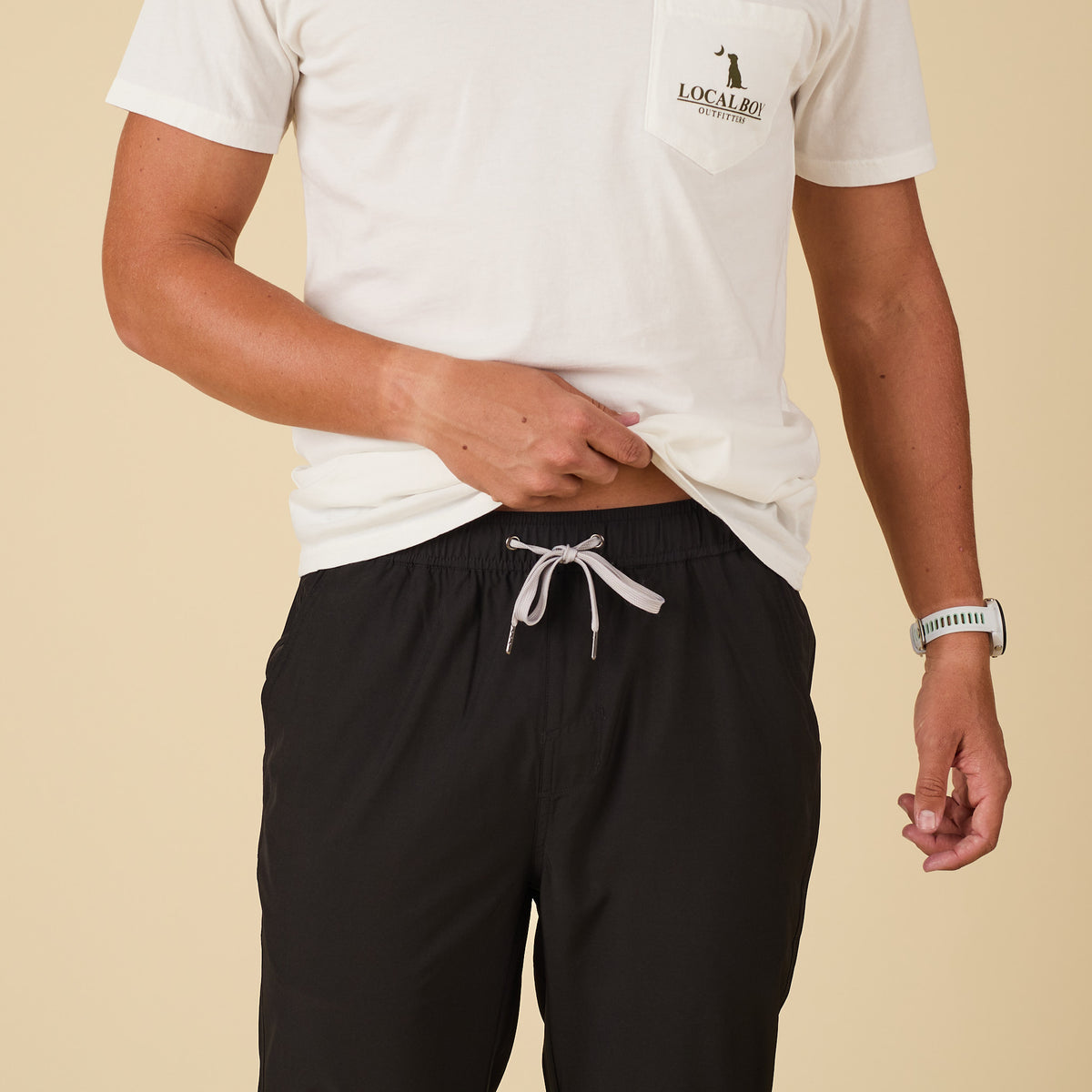 Person wearing a white t-shirt with a logo and black pants on a beige background