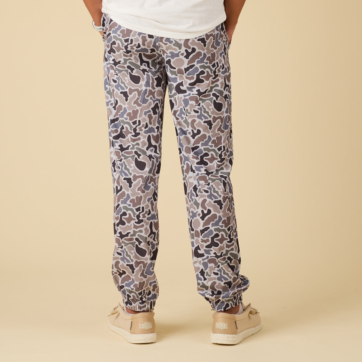 Camouflage-patterned jogger pants worn by a person on a beige background