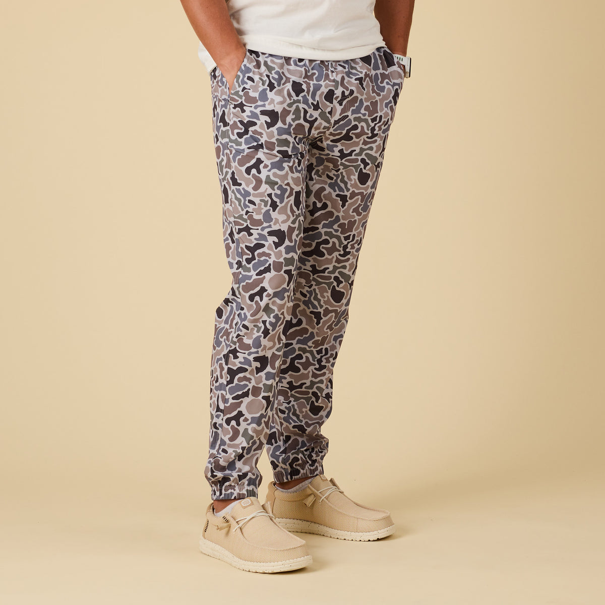 Person wearing camo jogger pants and beige shoes on a beige background