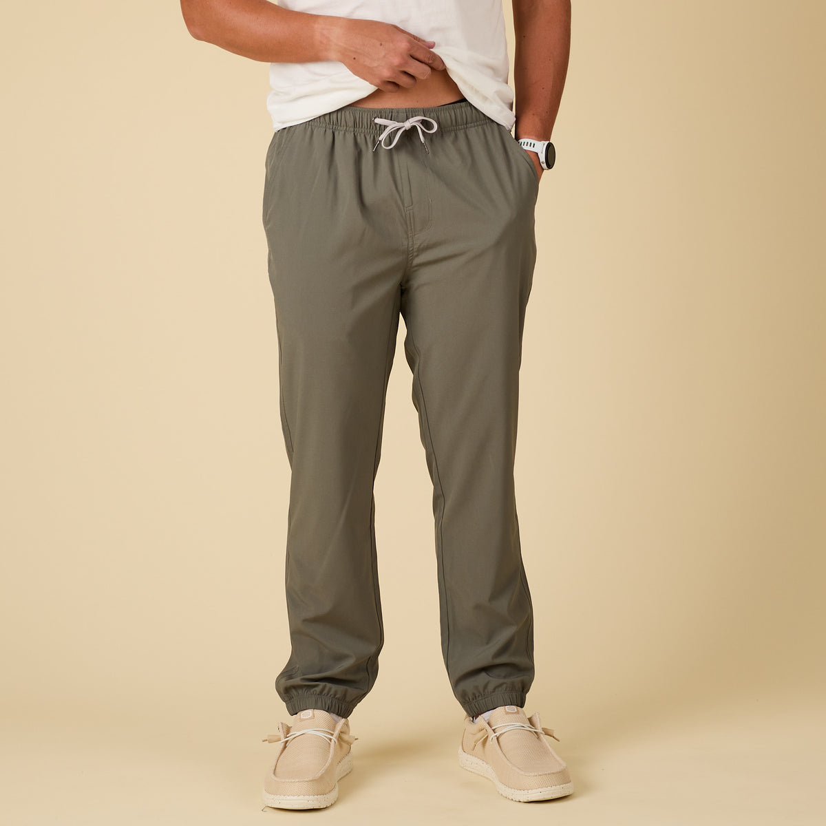 Person wearing olive green jogger pants on a beige background