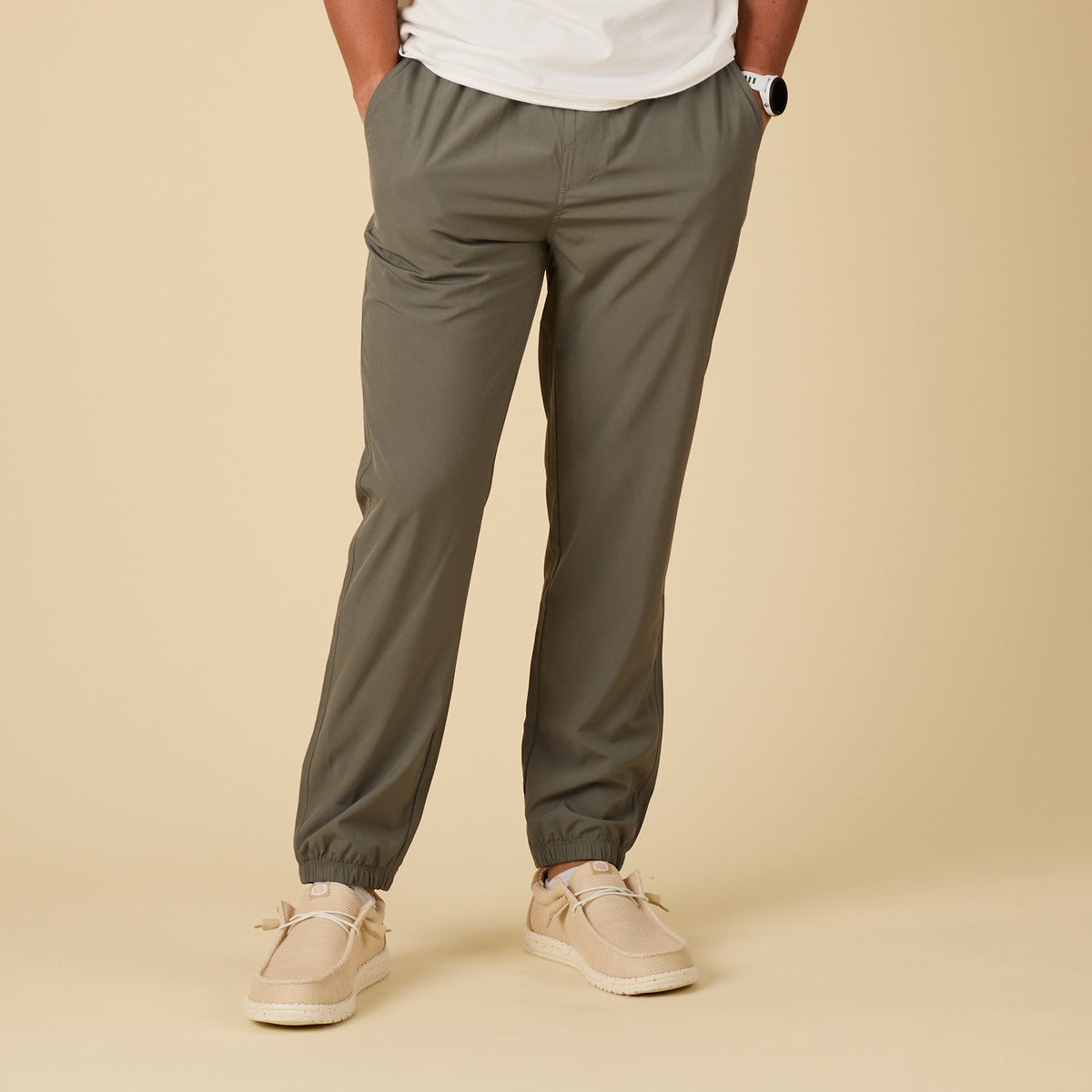 Person wearing olive green pants and beige shoes on a beige background