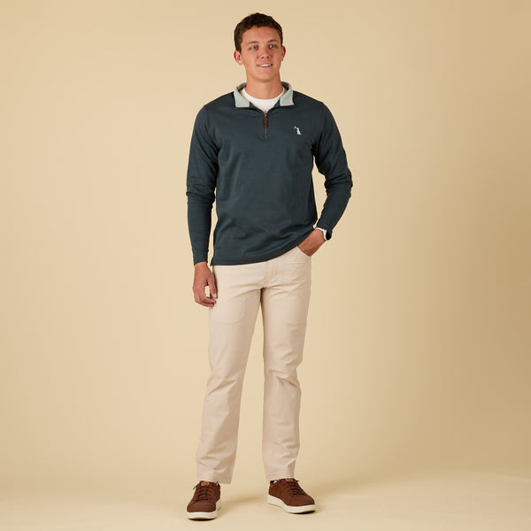 Man wearing a dark blue pullover with a logo, beige pants, and brown shoes on a beige background