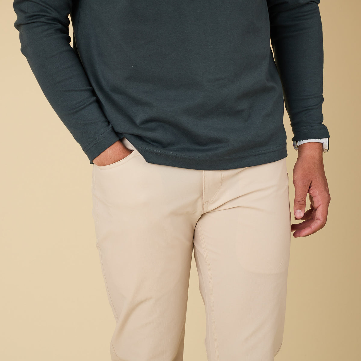 Person wearing a dark blue long-sleeve shirt and beige pants on a beige background