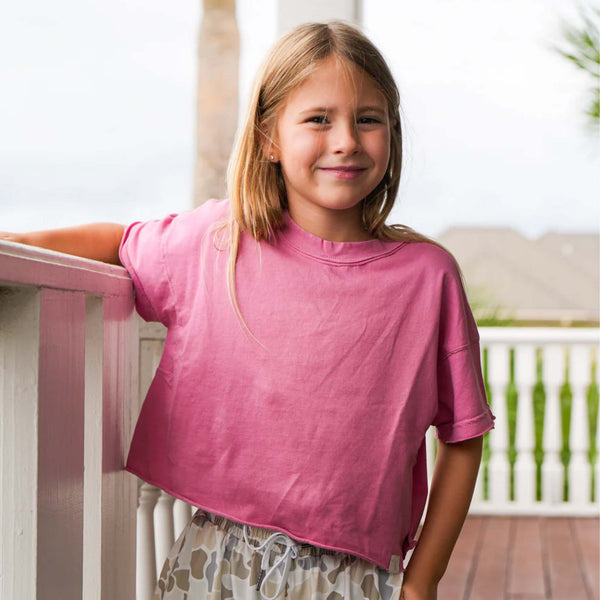 Young girl in a watermelon pink short sleeve boxy crop shirt standing on a porch