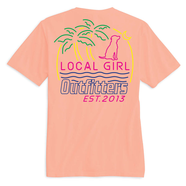 Back view of a neon cantaloupe-colored t-shirt featuring a vibrant tropical design with green palm trees, a pink silhouette of a dog, a yellow crescent moon, and the text “Local Girl Outfitters EST. 2013” in bold pink and purple lettering with wavy lines underneath.