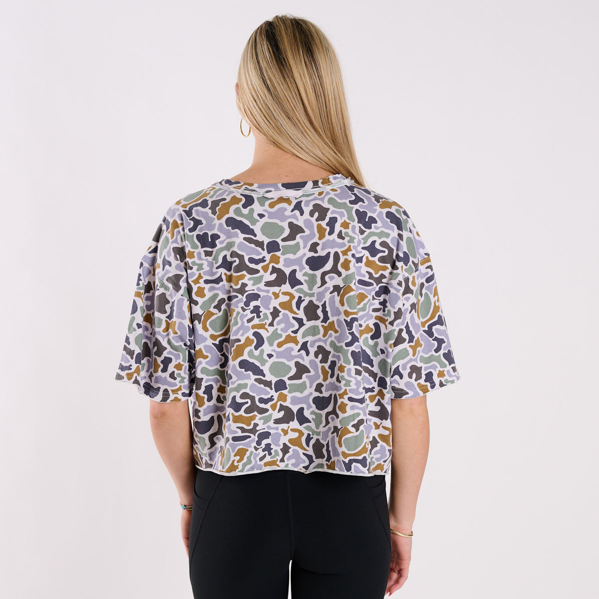 Woman wearing a boxy camo printed shirt on a grey background.