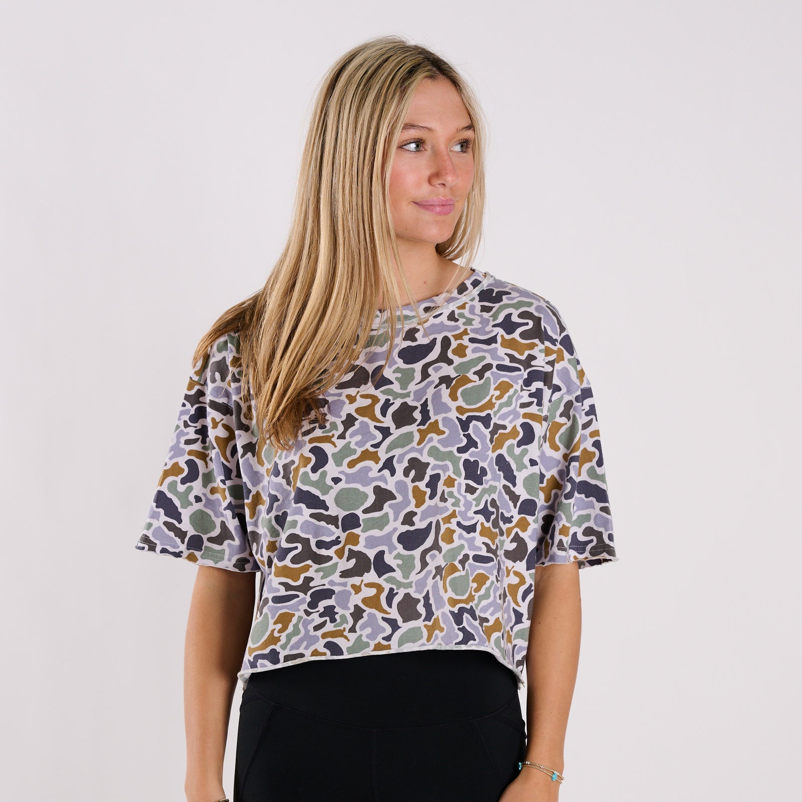 Woman wearing a boxy camo printed shirt on a grey background.
