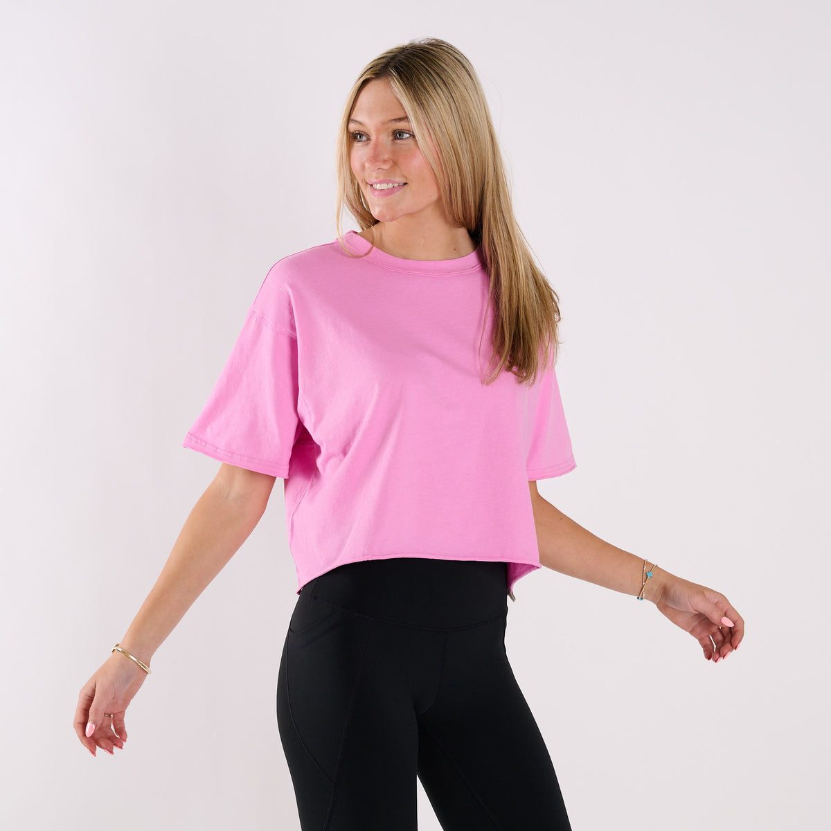Woman wearing a pink boxy crop t-shirt against a plain white background