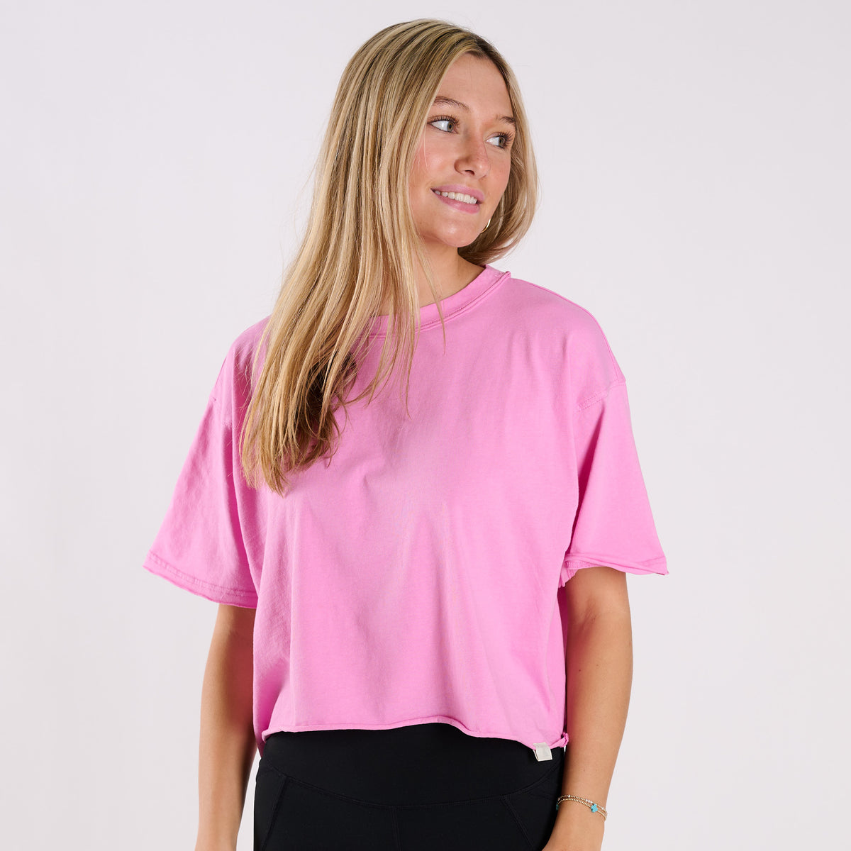 Woman wearing a pink boxy crop t-shirt against a plain white background
