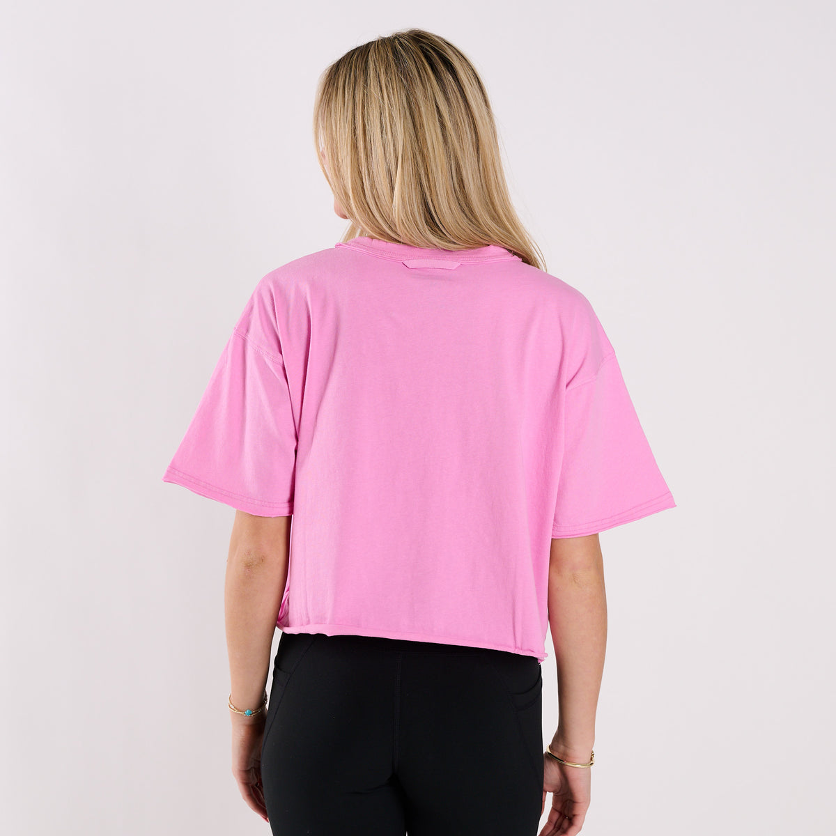 Woman wearing a pink boxy crop t-shirt against a plain white background