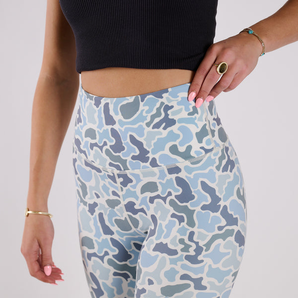 Close-up of waistband and side pocket detail on blue camo leggings with hand resting at hip.