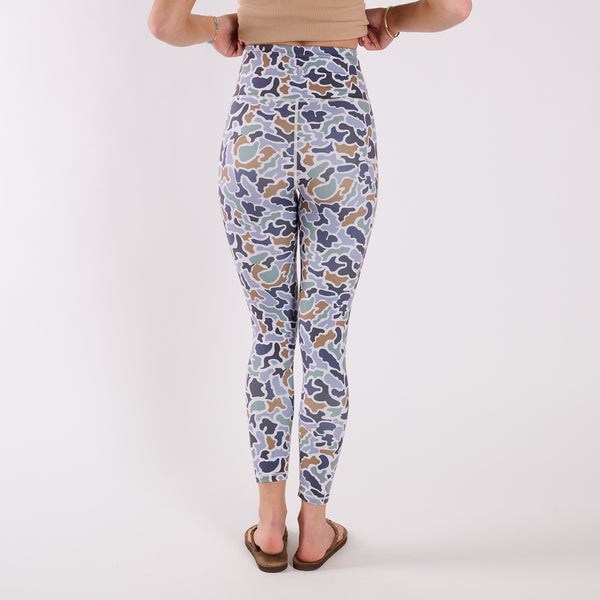 Back view of high-waisted camo leggings on model standing against white background, wearing flip flops.