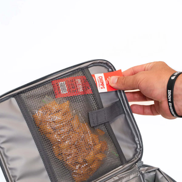 Burlebo lunchbox in classic deer camo with mesh interior pocket holding snacks and a hand reaching to insert a Chomps beef stick.