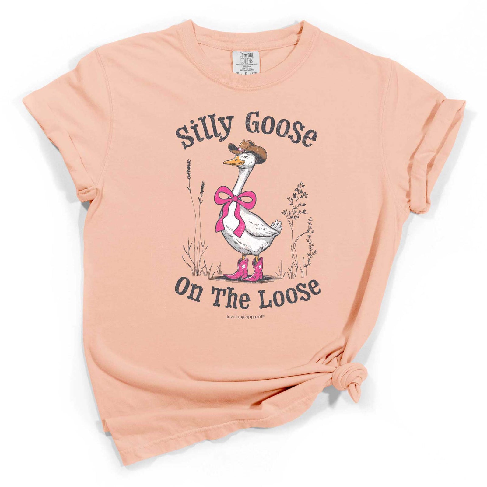 Peach short sleeve t-shirt with a graphic of a goose in cowgirl boots and bow, and text that reads “Silly Goose On the Loose.”