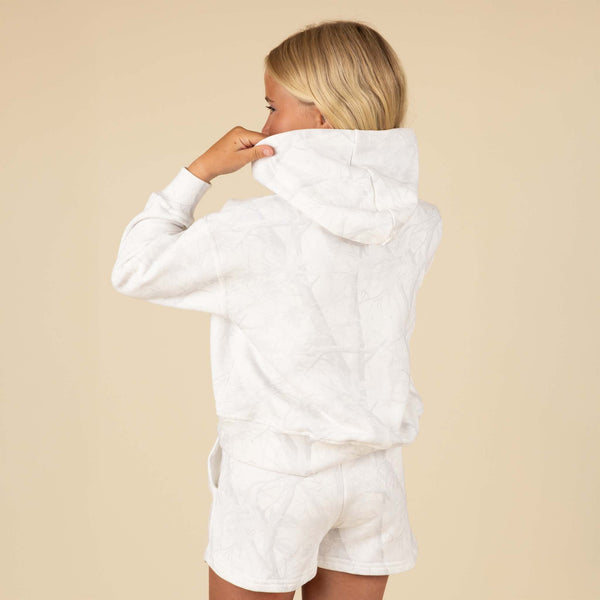 Girl adjusting the hood of a white tonal camo hoodie, shown from back and side angle.