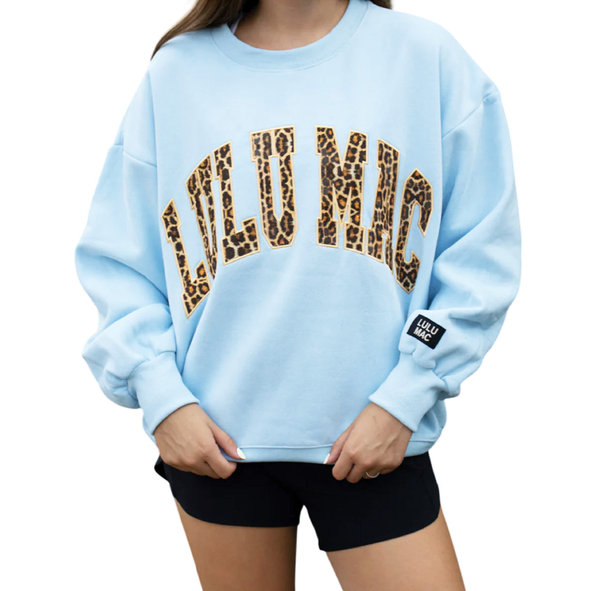 Light blue sweatshirt with leopard print text worn by a person on a white background