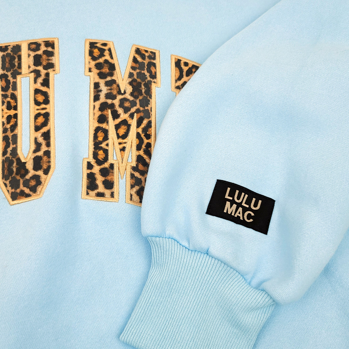 Light blue sweatshirt with 'LULU MAC' logo and leopard print letters on a light blue background