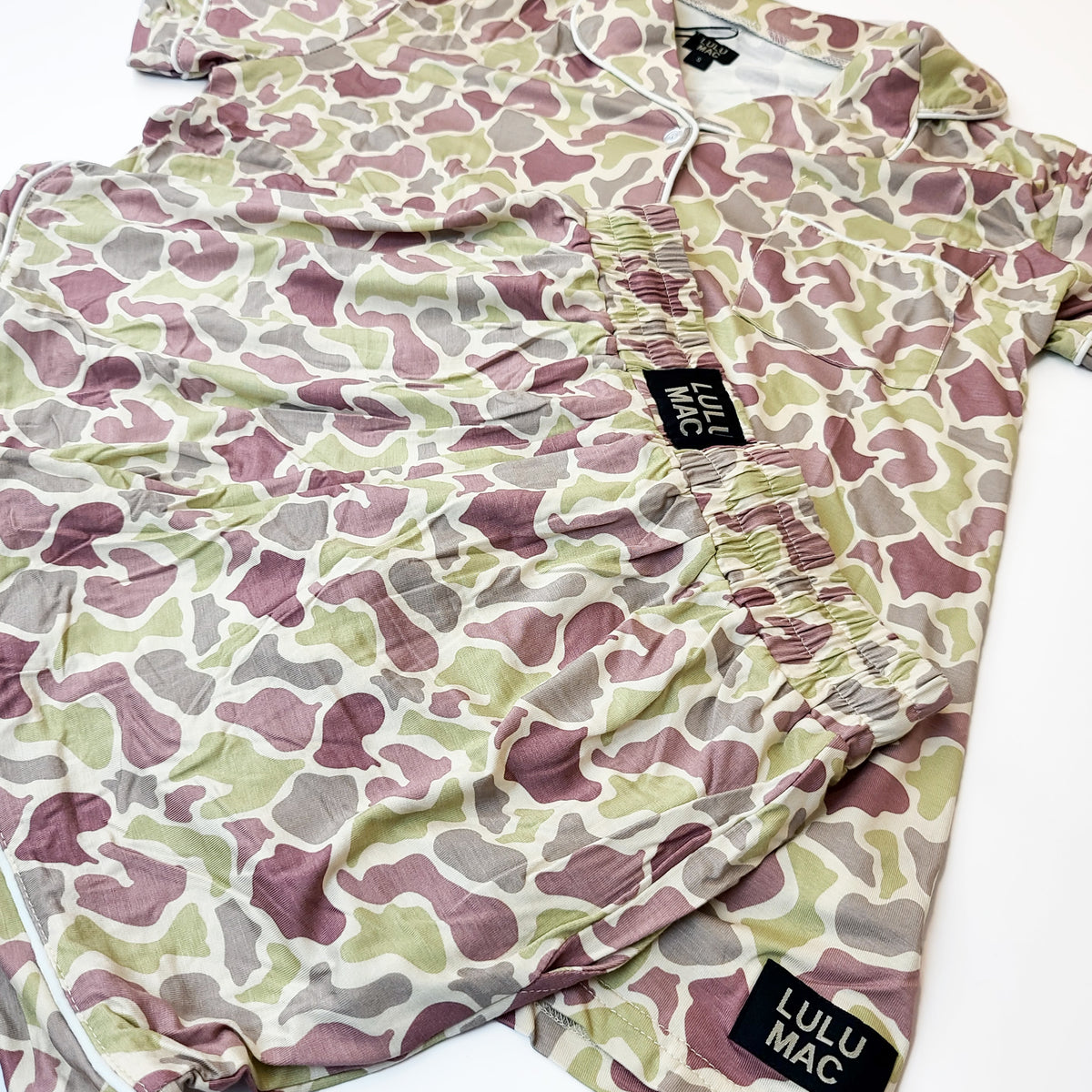 Close-up detail of Lulu Mac camo pajama set showing elastic waistband shorts, button-front top, and Lulu Mac logo tags.