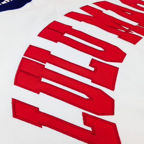 Close-up of Lulu Mac logo patch on sleeve and red, white, and blue ribbed cuff detail on white Lulu Mac sweatshirt.