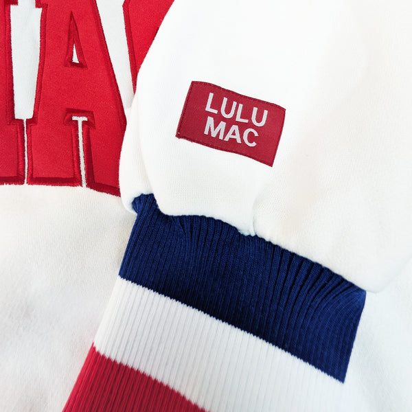 Close-up detail of red “LULU MAC” lettering stitched across the front of the white Lulu Mac crewneck sweatshirt.
